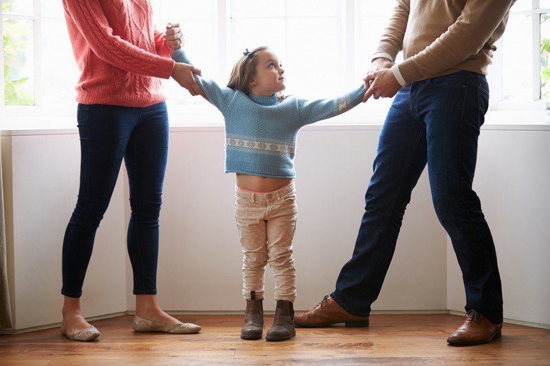 A man and woman are holding a little girl 's hand while standing next to each other.